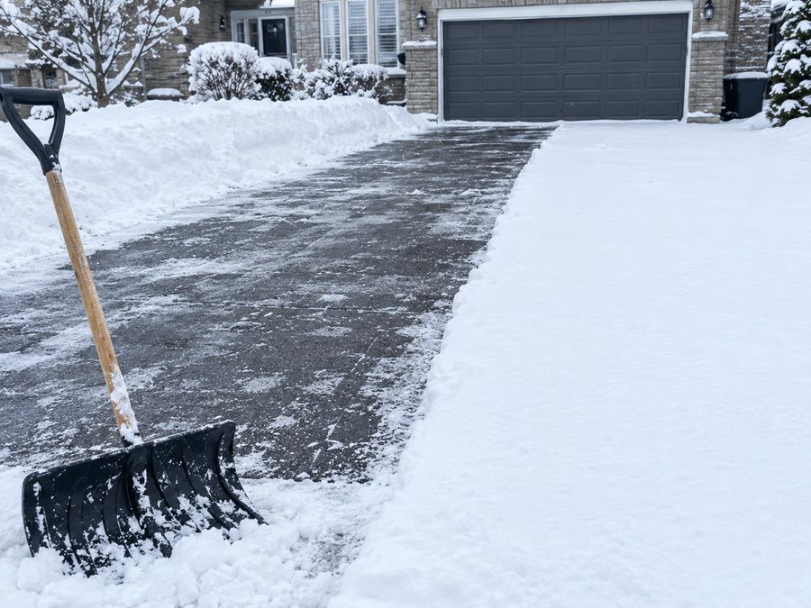 Snow cleared in front of the garage door and along the driveway with a shovel in the foreground