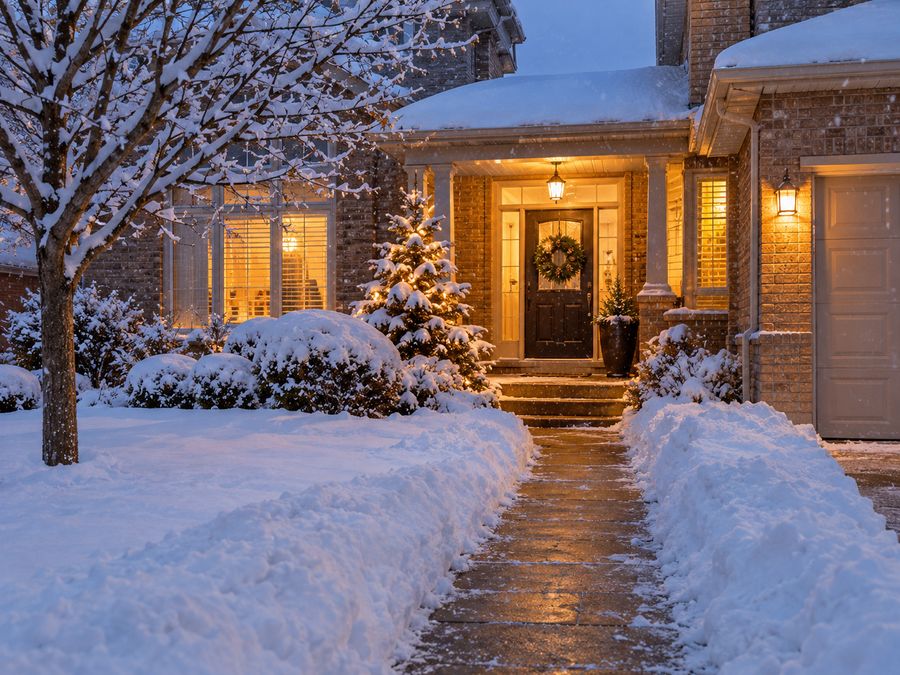 Warmly lit home entrance with a cleared walkway on a snowy evening