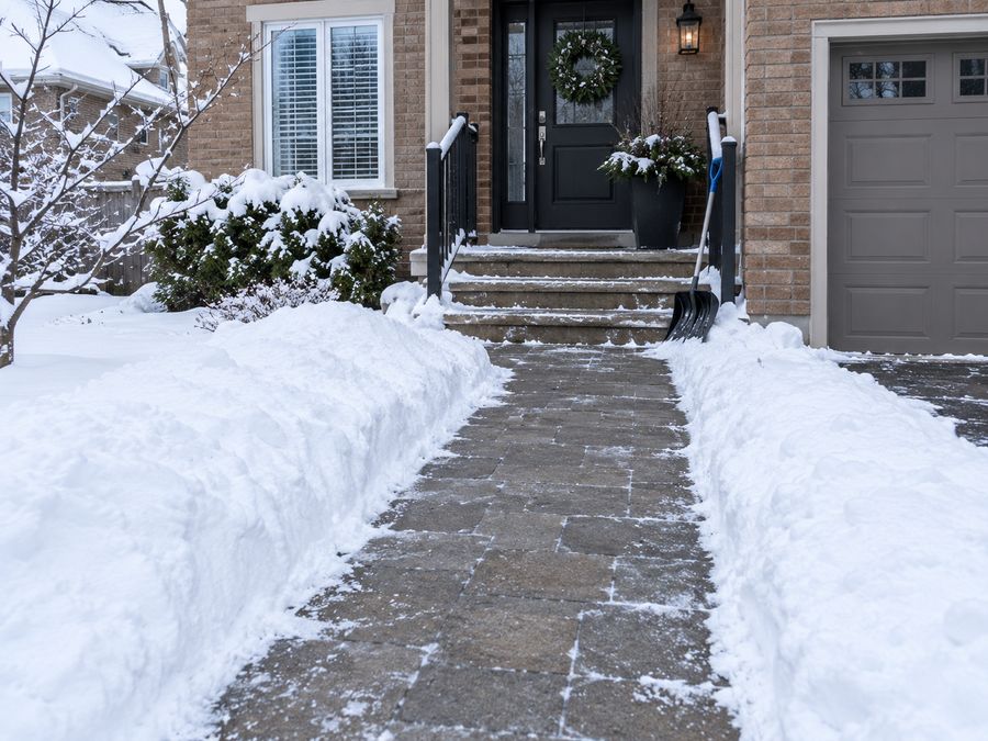 Shovelled front walkway and entrance steps with a snow shovel leaning by the door